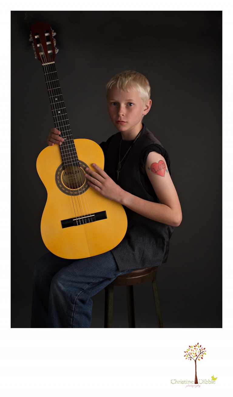 Sonora childrens photographer Christine Dibble Photography takes photos of a boy in studio black and white as he poses with an acoustic guitar.