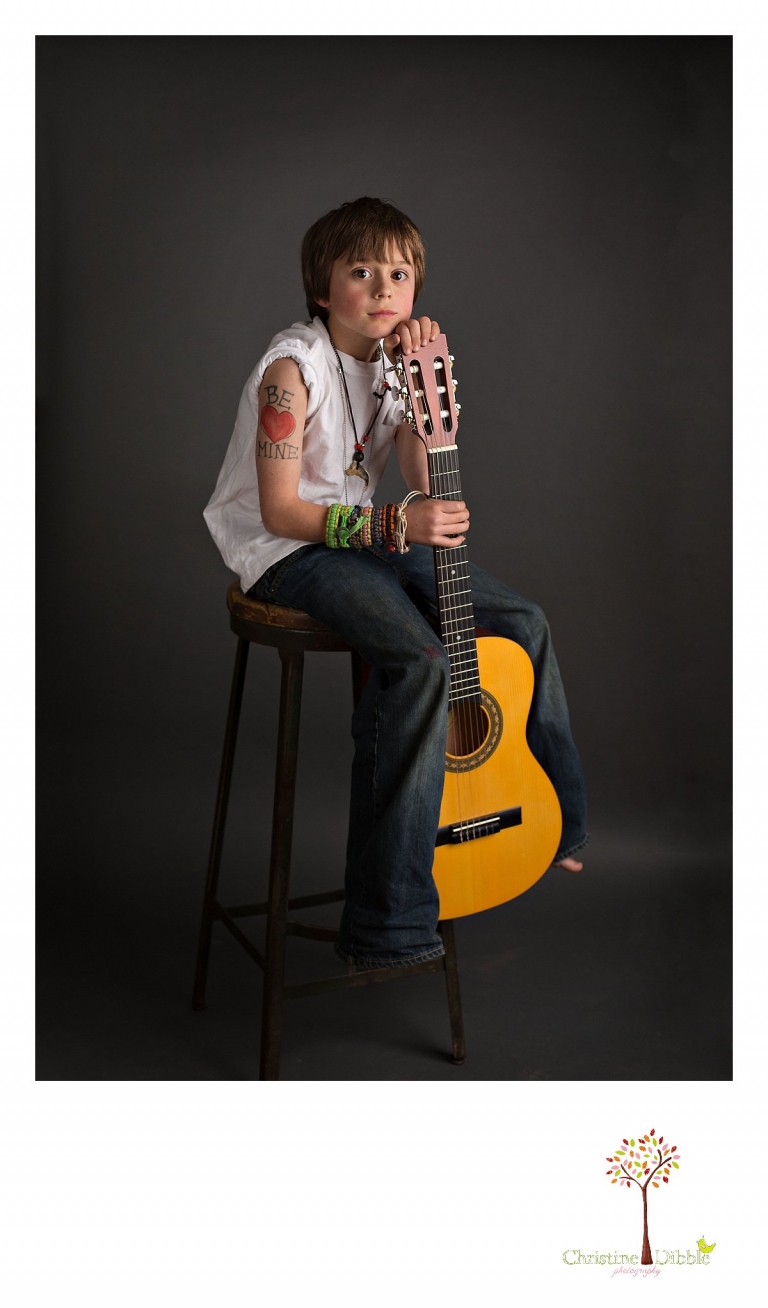 Sonora childrens photographer Christine Dibble Photography takes photos of a boy on a stool with an acoustic guitar in dramatic lighting.