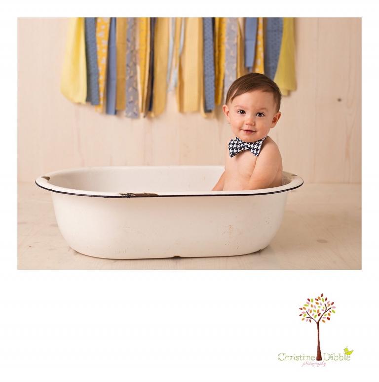 Sonora newborn and baby photographer Christine Dibble Photography takes photos of a baby boy as he smashes a cake for his first birthday with blues and yellows, fruit, and vintage crates and wash tubs.
