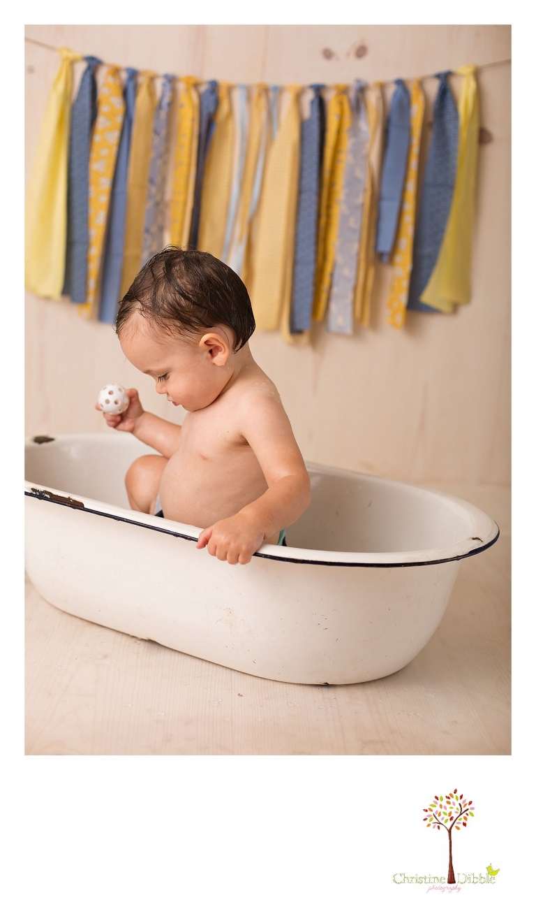 Sonora newborn and baby photographer Christine Dibble Photography takes photos of a baby boy as he smashes a cake for his first birthday with blues and yellows, fruit, and vintage crates and wash tubs.