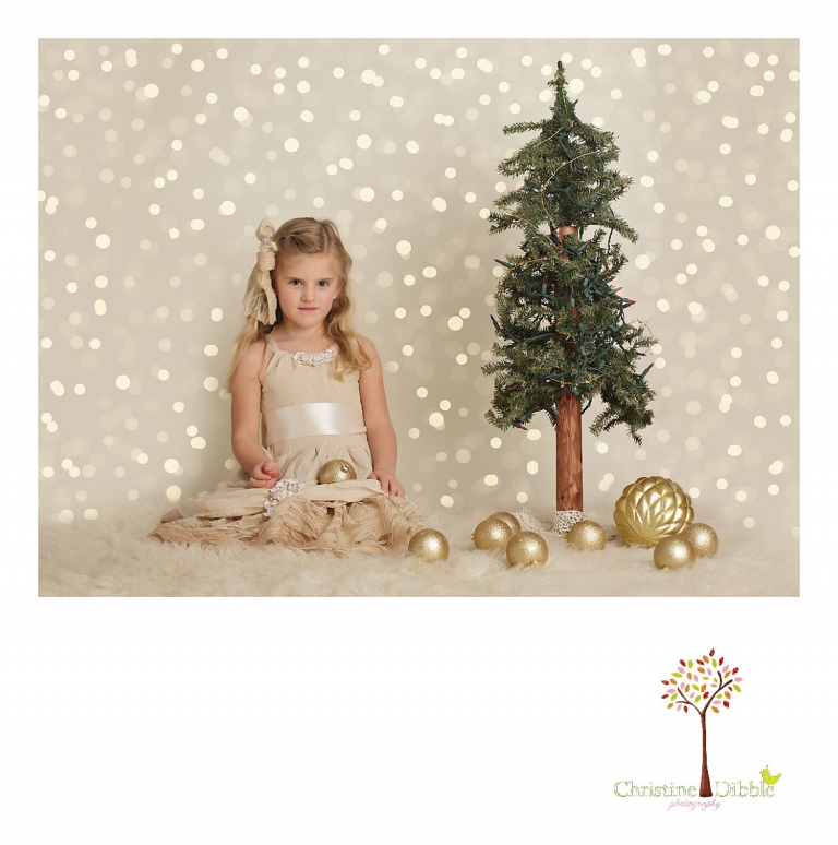 Sonora childrens photographer Christine Dibble Photography takes photos of a girl in a hand made flower girl dress created by Hopefully Romantic as she sits with a Christmas tree in front of bokeh lights.