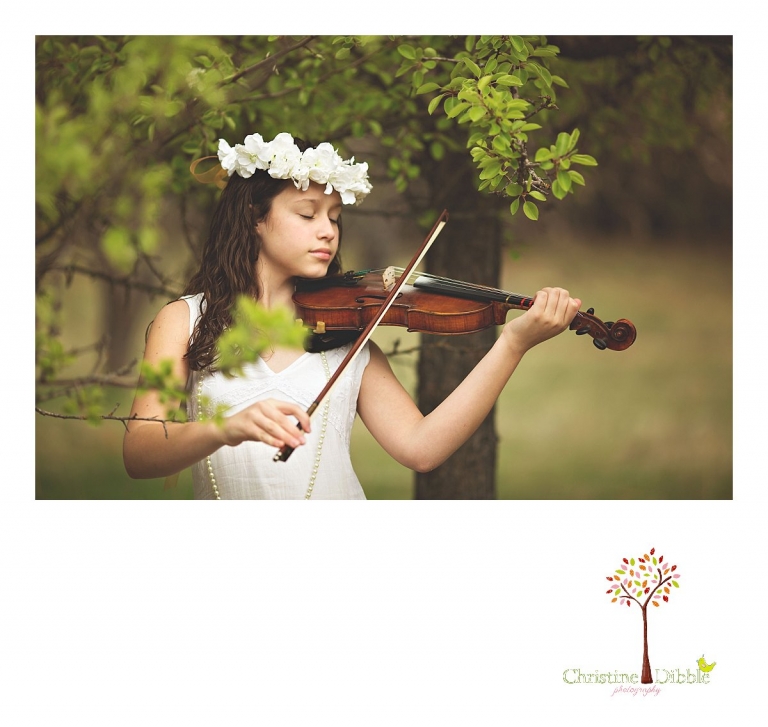 Sonora childrens photographer Christine Dibble Photography takes photos of a girl as she plays her violin under a blossoming apple tree while wearing a flower head wreath.