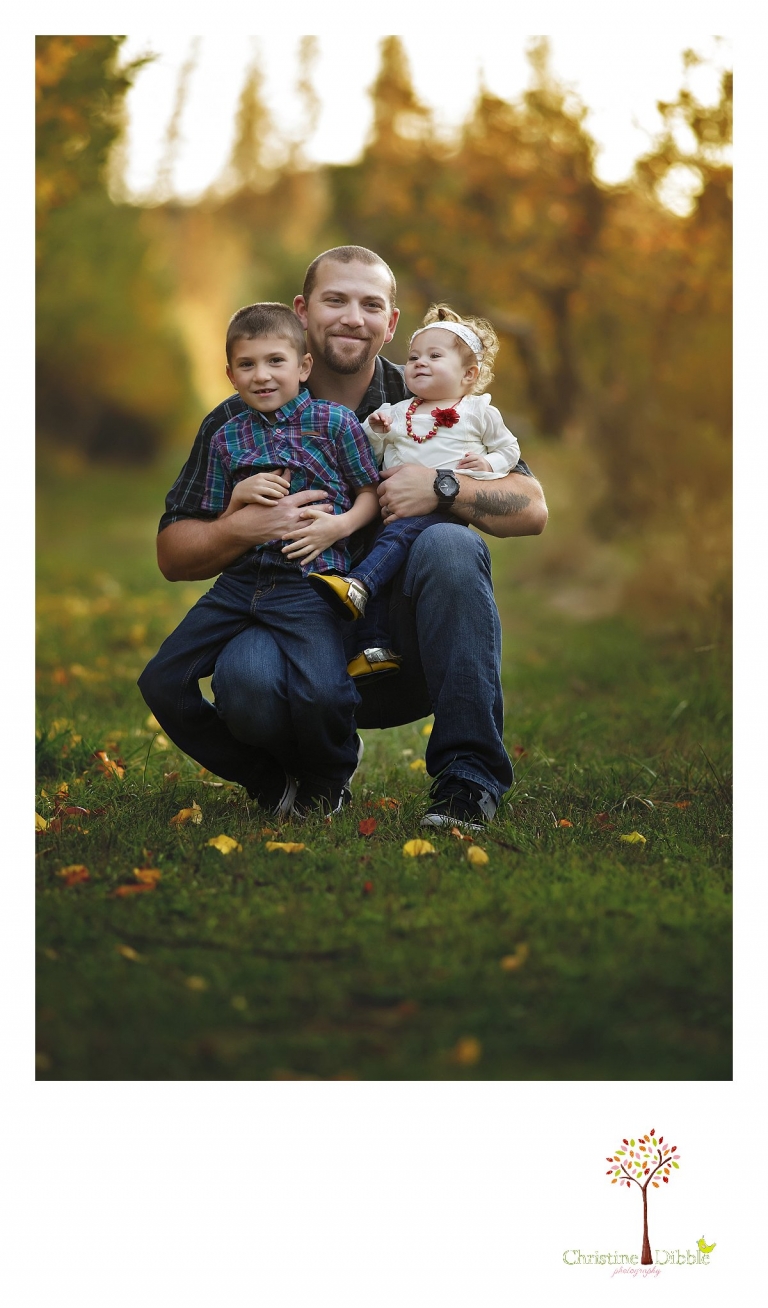 Dad holds his two young children during a Sonora family photography session photographed by Christine Dibble Photography at Indigeny Reserve in the fall among the apple orchards.