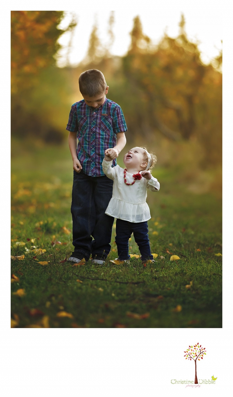 Little sister looks up at her big brother during a Sonora family photography session photographed by Christine Dibble Photography at Indigeny Reserve in the fall among the apple orchards.