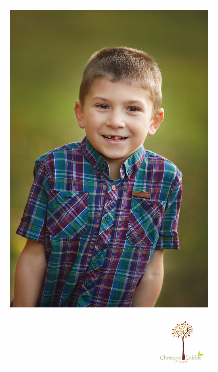 A young boy poses for a photo during a Sonora family photography session photographed by Christine Dibble Photography at Indigeny Reserve in the fall among the apple orchards.