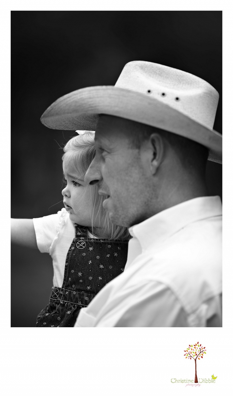 A cowboy holds his baby girl and points out horses at Aspen Meadows Pack Station while Christine Dibble Photography takes a black and white photo.