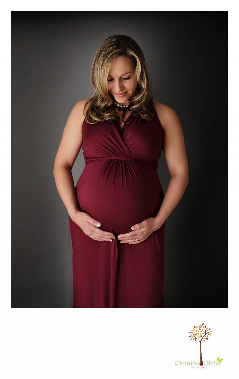 Sonora Maternity Photographer Christine Dibble Photography takes indoor photos during a maternity photography session showing the baby belly bump in dramatic lighting and a beautiful red dress.