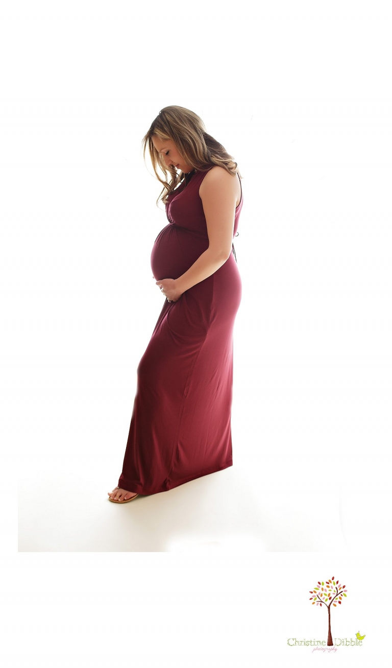 Sonora Maternity Photographer Christine Dibble Photography takes indoor photos during a maternity photography session showing the baby belly bump in dramatic lighting and a beautiful red dress.