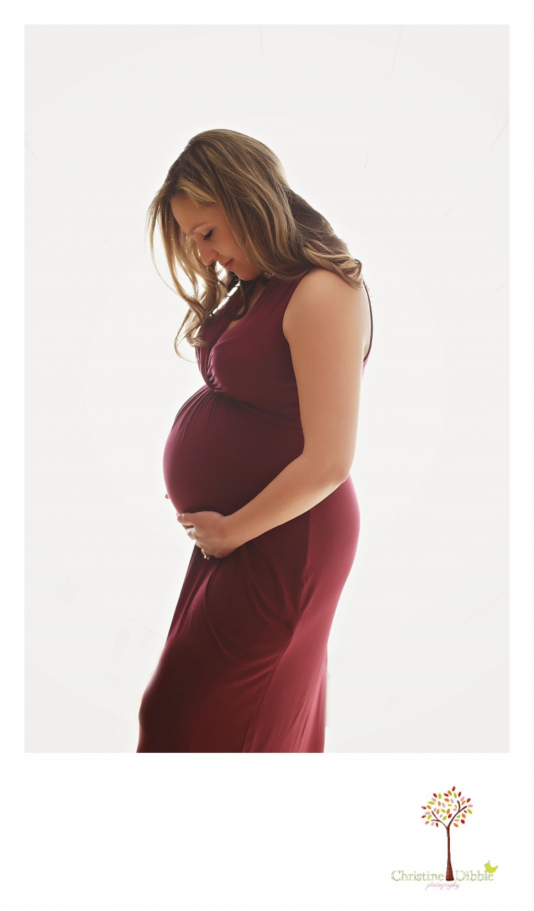 Sonora Maternity Photographer Christine Dibble Photography takes indoor photos during a maternity photography session showing the baby belly bump in dramatic lighting and a beautiful red dress.