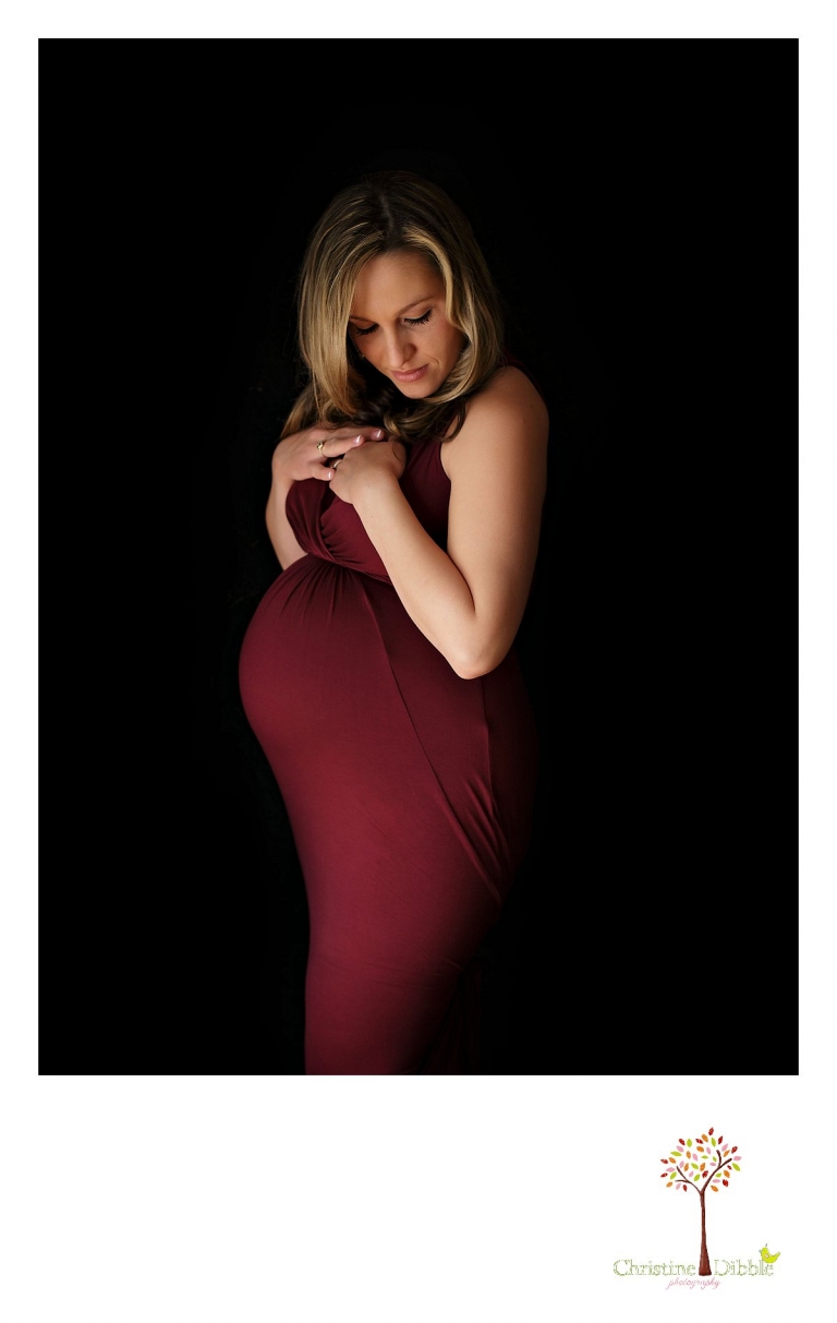 Sonora Maternity Photographer Christine Dibble Photography takes indoor photos during a maternity photography session showing the baby belly bump in dramatic lighting and a beautiful red dress.