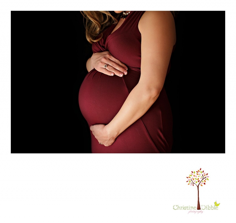 Sonora Maternity Photographer Christine Dibble Photography takes indoor photos during a maternity photography session showing the baby belly bump in dramatic lighting and a beautiful red dress.
