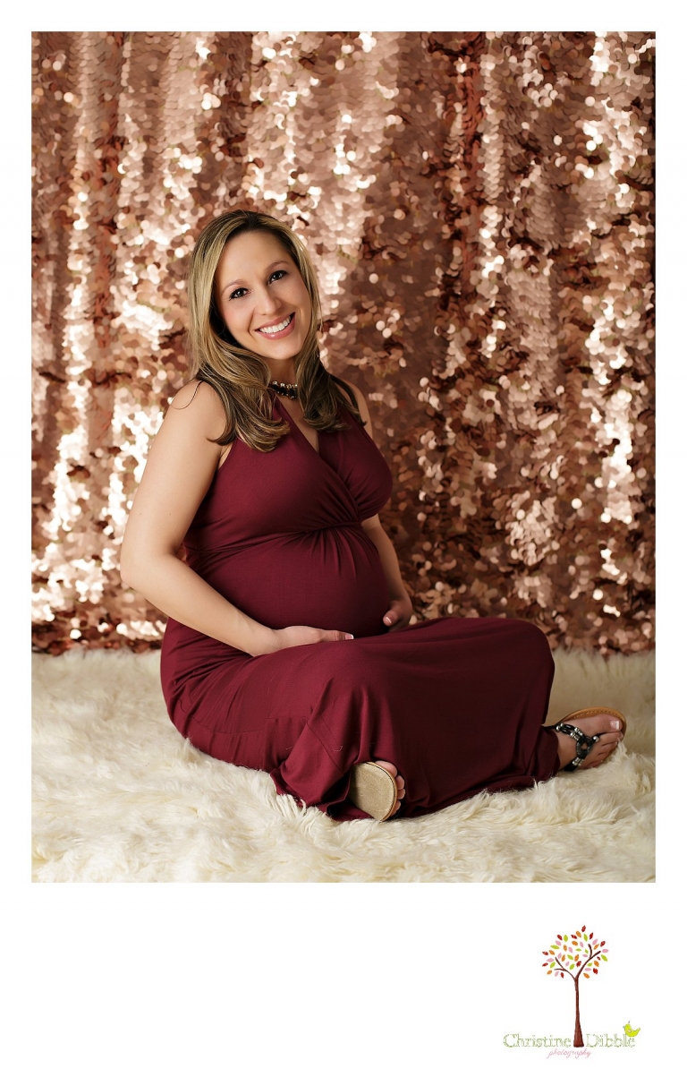 Sonora Maternity Photographer Christine Dibble Photography takes indoor photos during a maternity photography session showing the baby belly bump in dramatic lighting and a beautiful red dress.