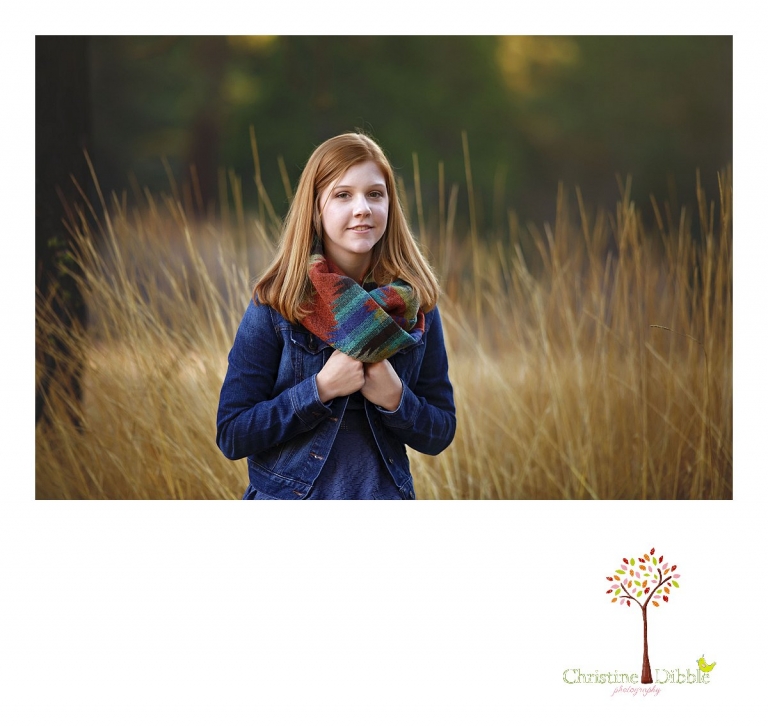 Sonora and Turlock senior portrait photographer Christine Dibble Photography takes outdoor fall senior photos of a girl in a denim jacket and scarf in a field with tall grass behind her.
