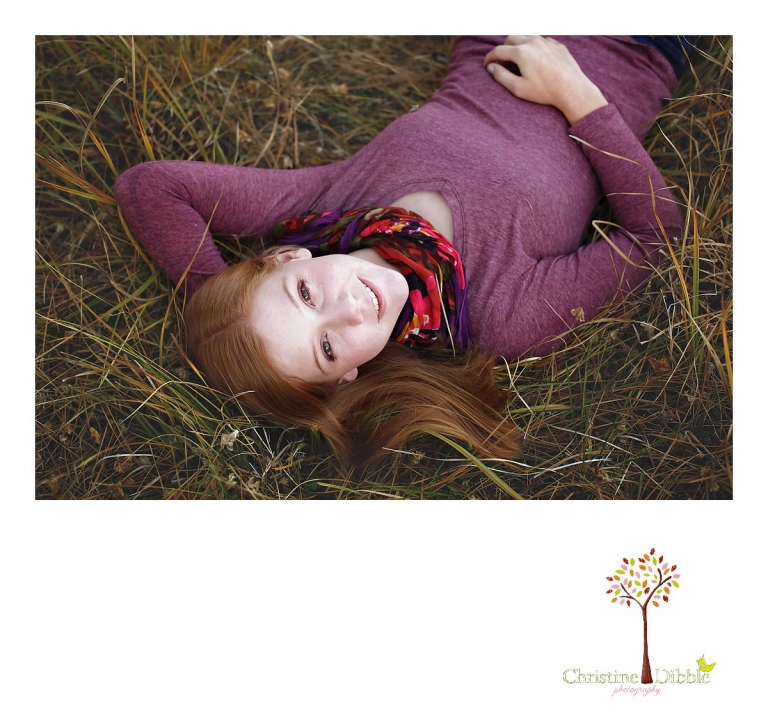 Sonora and Turlock senior portrait photographer Christine Dibble Photography takes outdoor fall senior photos of a girl lying in a field of grass while wearing purple and a floral scarf.