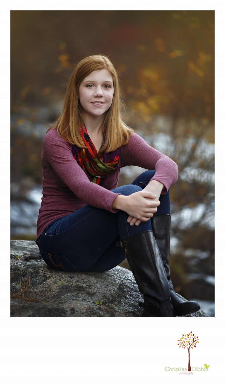 Sonora and Turlock senior portrait photographer Christine Dibble Photography takes outdoor fall senior photos of a girl on a rock in the river with fall haze behind her.