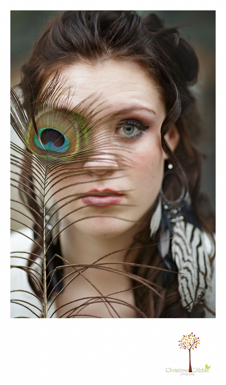 Sonora, CA senior model photographer Christine Dibble takes outdoor modeling photos of a teenage girl for a modeling portfolio while she holds a peacock feather over one eye.