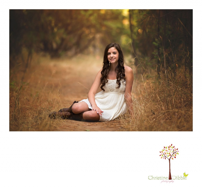 Sonora, Summerville and Turlock senior portrait photographer Christine Dibble Photography takes outdoor senior photos of a senior girl in a white sundress sitting on a path in a grove of trees in a field.