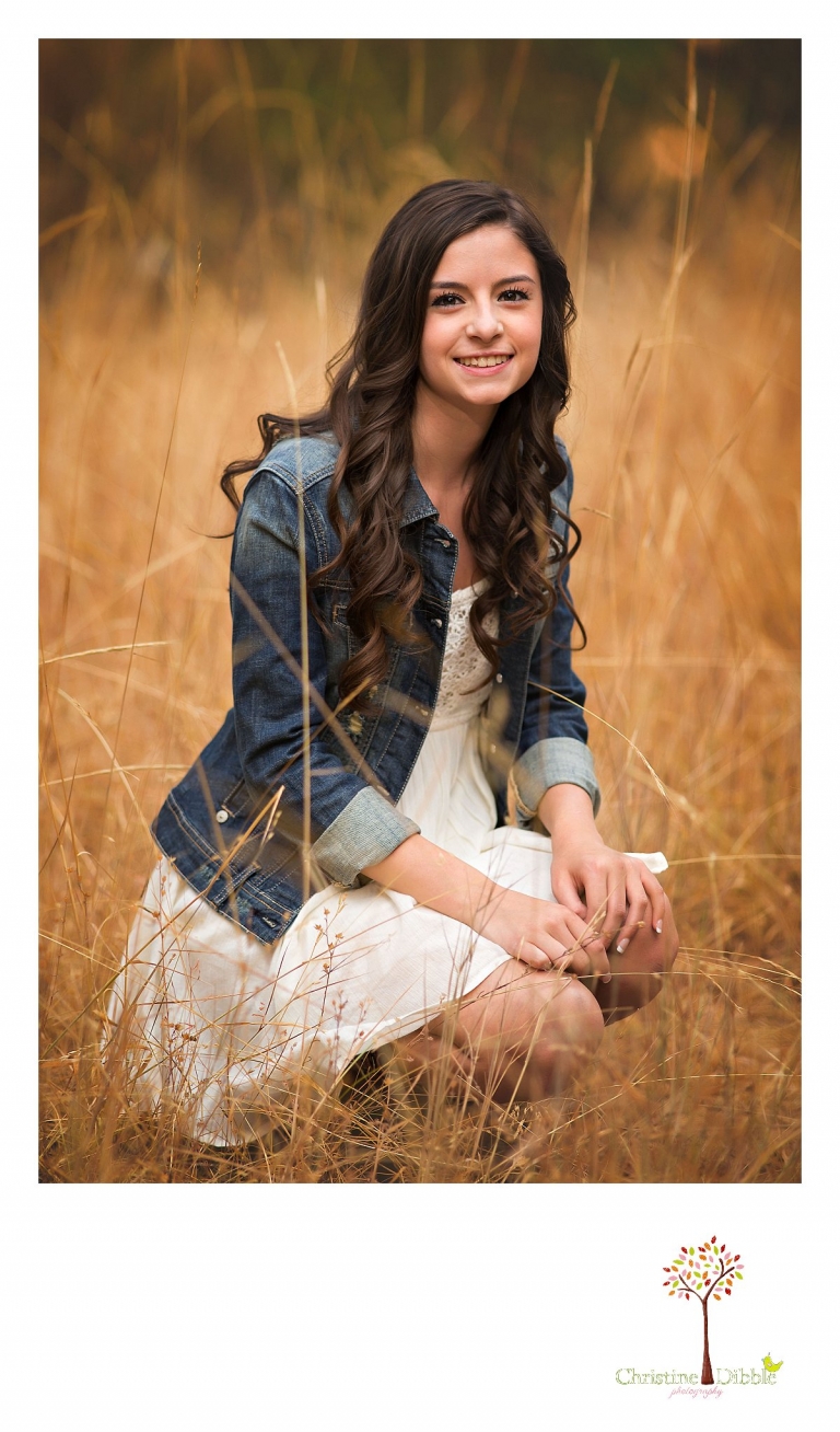 Best Sonora, Summerville and Turlock senior portrait photographer Christine Dibble Photography takes outdoor senior photos of a girl in a white dress and jean jacket  in a field.