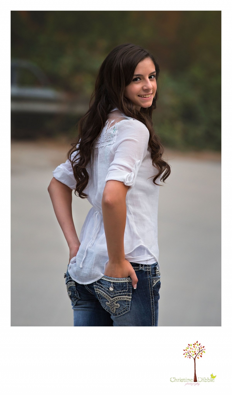 Sonora, Summerville and Turlock senior portrait photographer Christine Dibble Photography takes outdoor senior photos of a girl looking backwards with her hands in the back pockets of her Miss Me jeans.