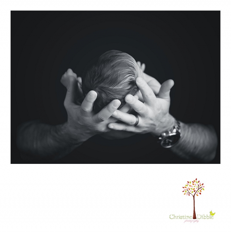 A black and white image of a baby girl's head in dad's hands is taken during a Sonora, CA newborn photography session by best Sonora newborn photographer Christine Dibble Photography.