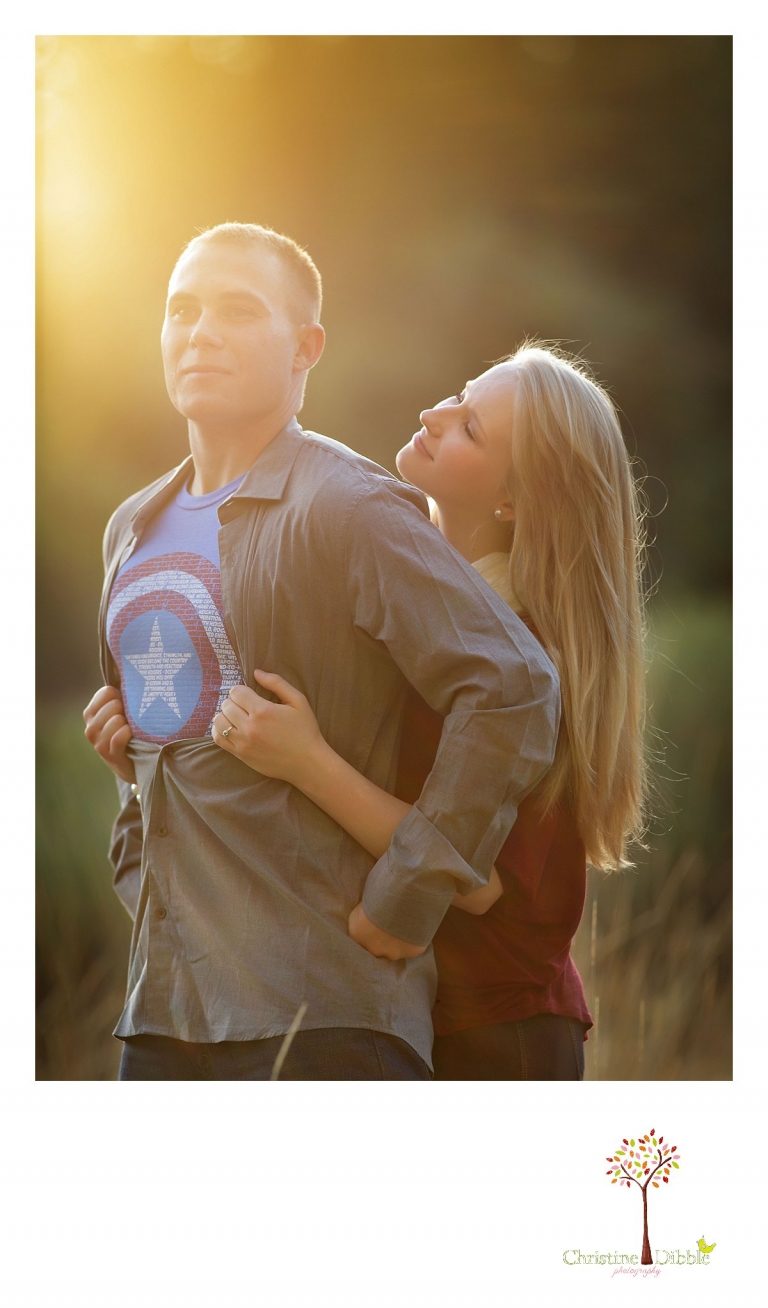 Sonora, CA couple's and engagement photographer Christine Dibble Photography takes romantic engagement style photos of a couple in a field as they pose super hero style in a Captain America t-shirt.