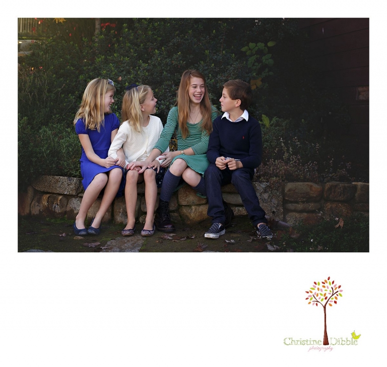 Christine Dibble Photography, best Sonora family photographer, takes outdoor portraits of a blended family's new siblings sitting on a stone wall  in their renovated backyard in Tuolumne.