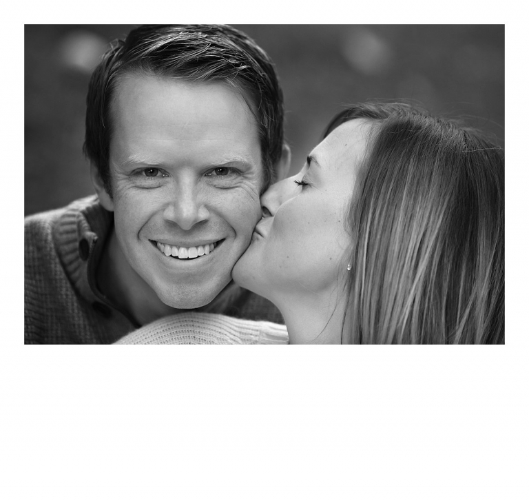 A wife kisses her husband as he smiles for a black and white photo taken during a Sonora, CA family photography session at Indigeny Reserve by Christine Dibble Photography in the fall.