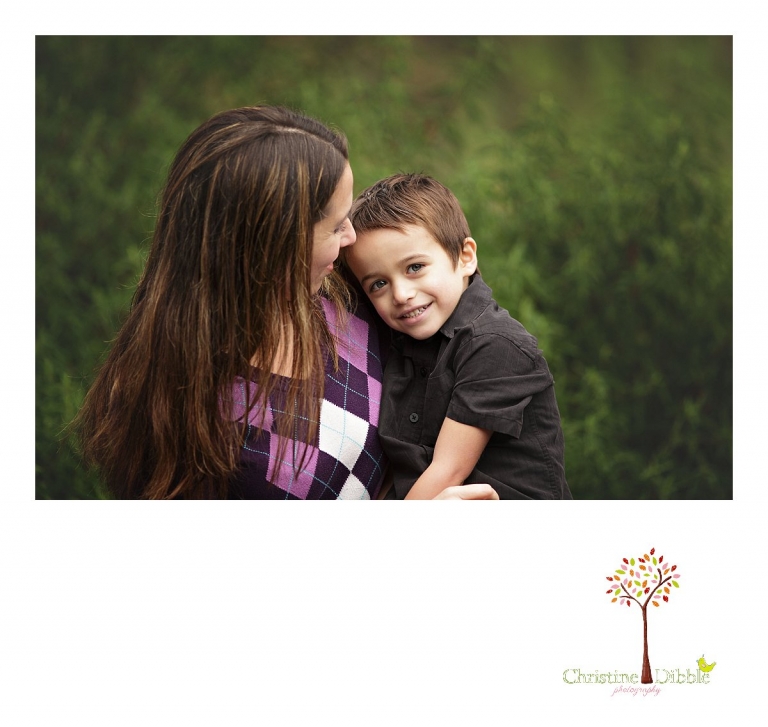 Sonora photographer Christine Dibble Photography takes a photo of a shy young boy looking at the camera from mom's hug during a  four generation family portraits outside on a foggy morning in the clients' yard.