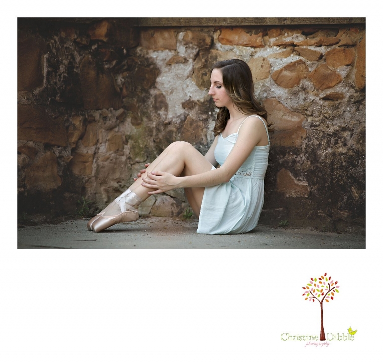 A dancer sits with toes on pointe by a rock wall at Kbnights Ferry as Summerville and Sonora High senior portrait photographer Christine Dibble Photography takes a portrait.