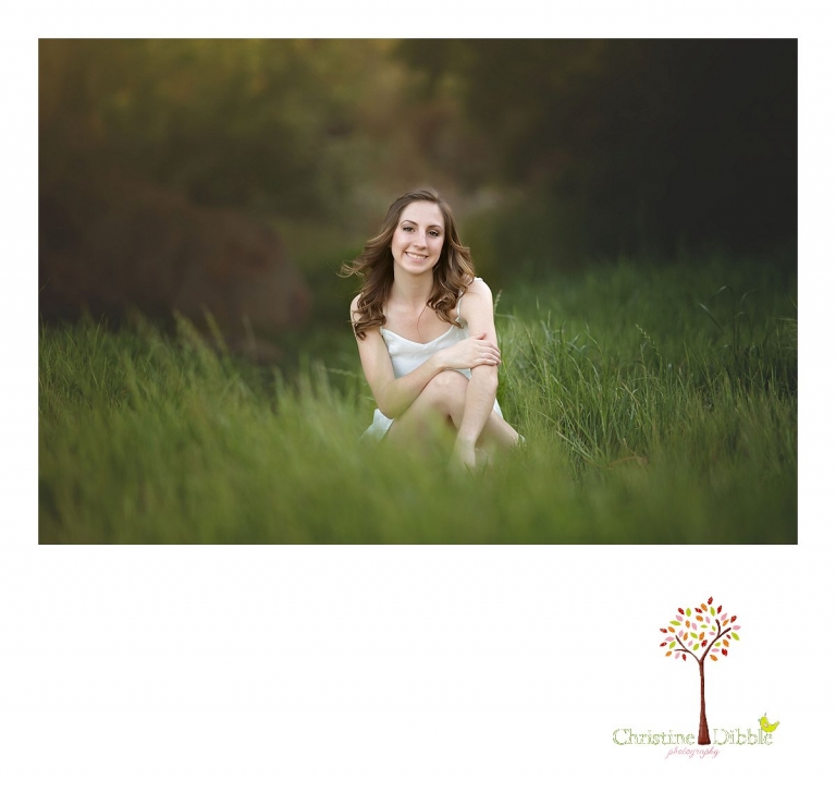 Summerville and Sonora High senior portrait photographer Christine Dibble Photography takes a photo of a girl sitting in green grass with sunflare behind her at Knights Ferry.
