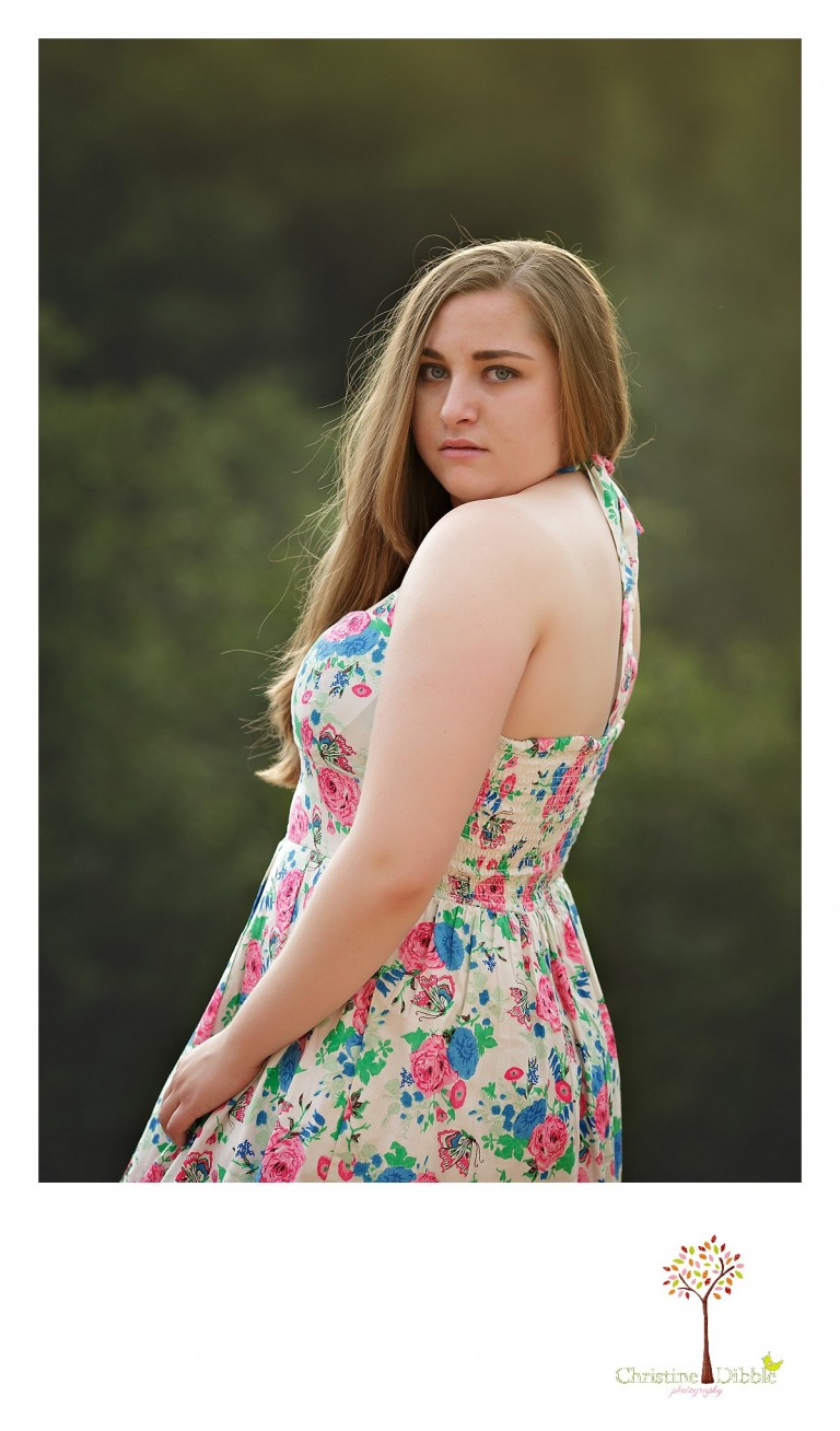 A senior girl looks over her shoulder at the camera while lit from behind by the sun as a portrait is taken by Sonora High senior portrait photographer Christine Dibble Photography.