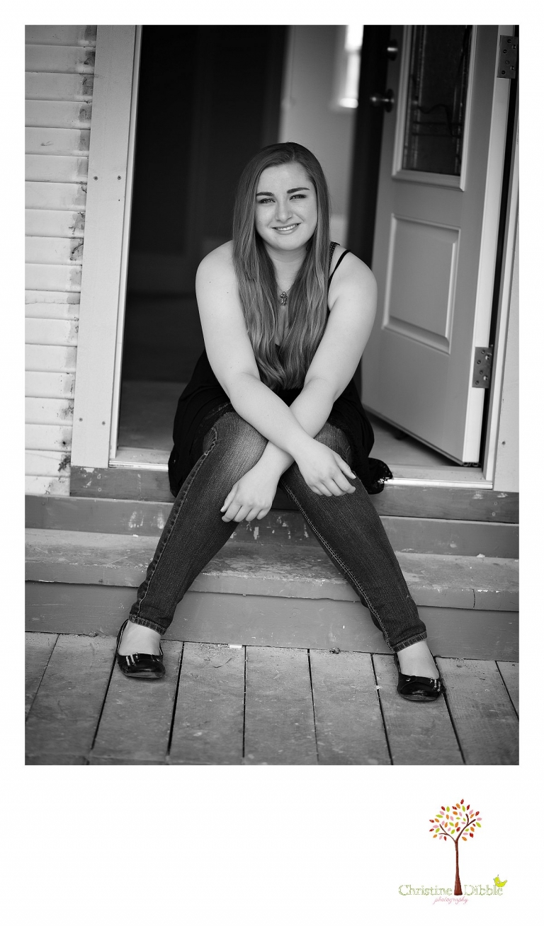 Sonora High senior portrait photographer Christine Dibble Photography takes a black and white photo of a senior girl sitting in the doorway of an old house in Jamestown.
