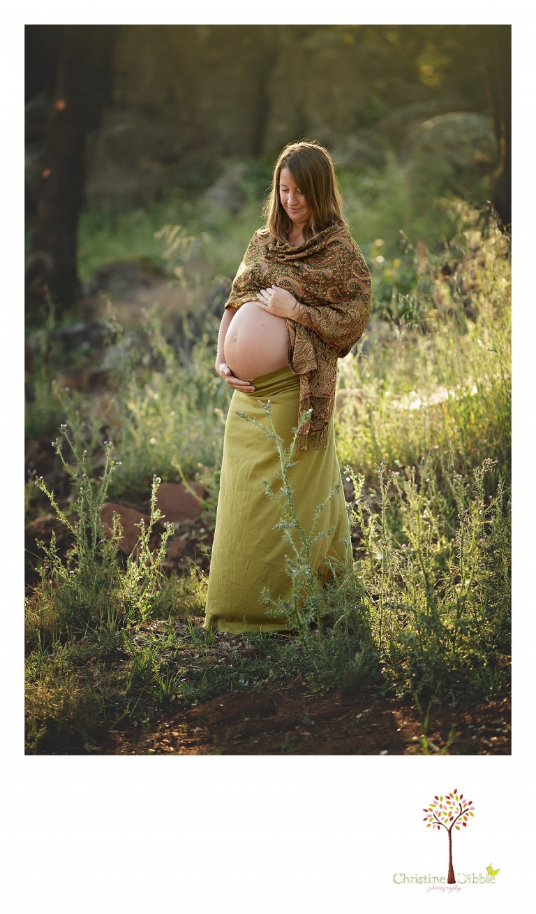 Sonora maternity photographer Christine Dibble Photography takes pregnancy and maternity photos of a mother wearing greens, browns and golds as she stands in golden sunlight with her hands on her bare pregnant belly baby bump.