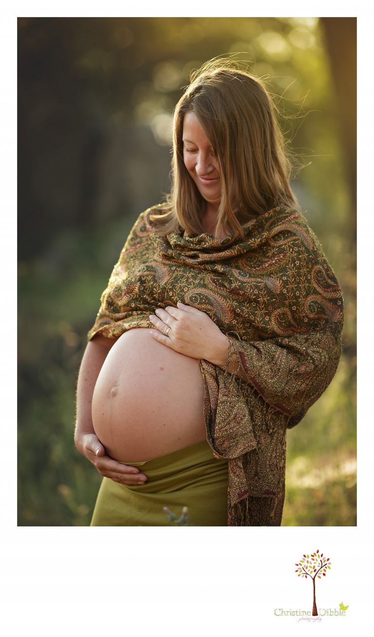 Sonora maternity photographer Christine Dibble Photography takes beautiful golden hour portraits of a mom-to-be looking down at her pregnant belly as she wears greens, golds and browns.