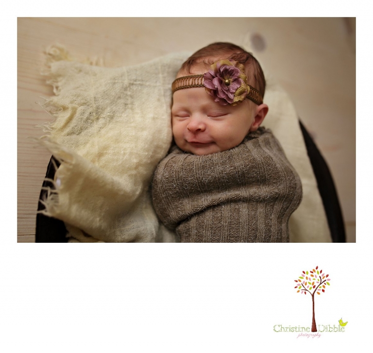 Best Sonora newborn photographer Christine Dibble Photography takes indoor studio photos of a newborn baby girl sleeping in a wooden bowl while wearing a flowered headband.