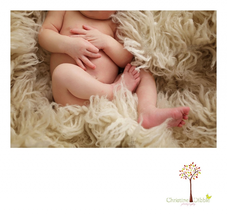 Best Sonora newborn photographer Christine Dibble Photography takes indoor studio photos of a newborn baby girl's peeling hands and feet as she sleeps on a cream colored Flokati rug.