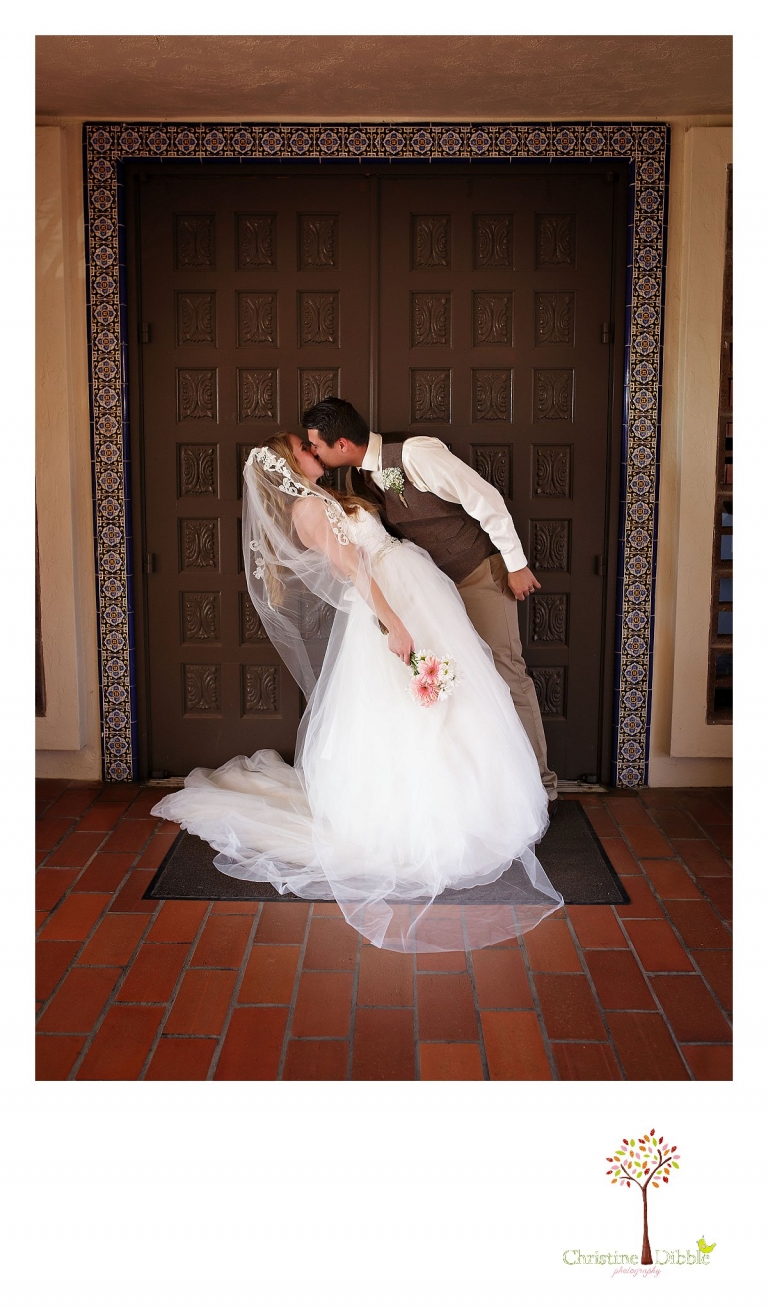 The bride and groom dip and kiss in front of an ornate wooden door at the Don Pedro Hacienda as Sonora wedding photographer Christine Dibble Photography takes a photo.