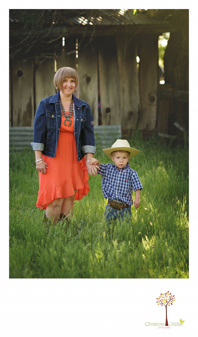Sonora child photography by Christine Dibble Photography captures a three year old boyholding mom's hand in a grass field near a rustic building.
