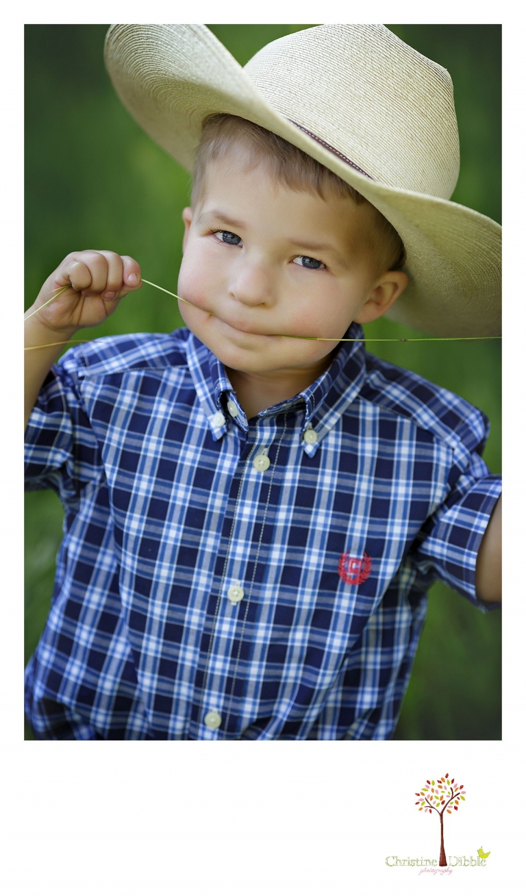 Sonora child photography by Christine Dibble Photography captures a three year old boy as he chews grass while wearing a cowboy hat.