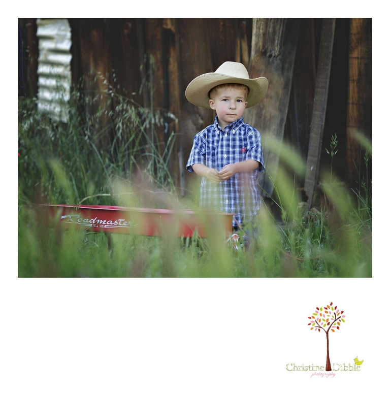 Sonora child photography by Christine Dibble Photography captures a three year old cowboy in tall grass near a rustic ranch building.