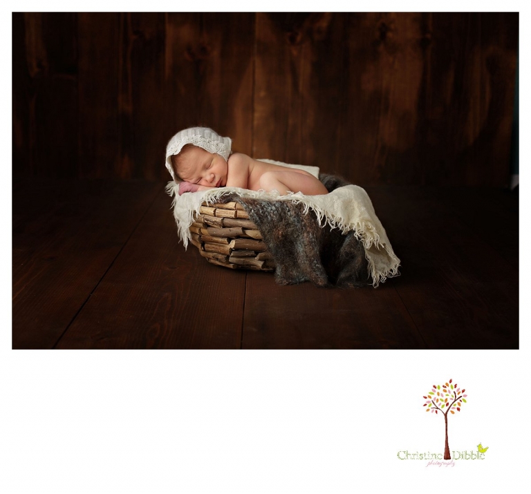 Sonora newborn photographer Christine Dibble Photography takes photos of a baby girl as she sleeps in a wooden bowl wearing a bonnet.