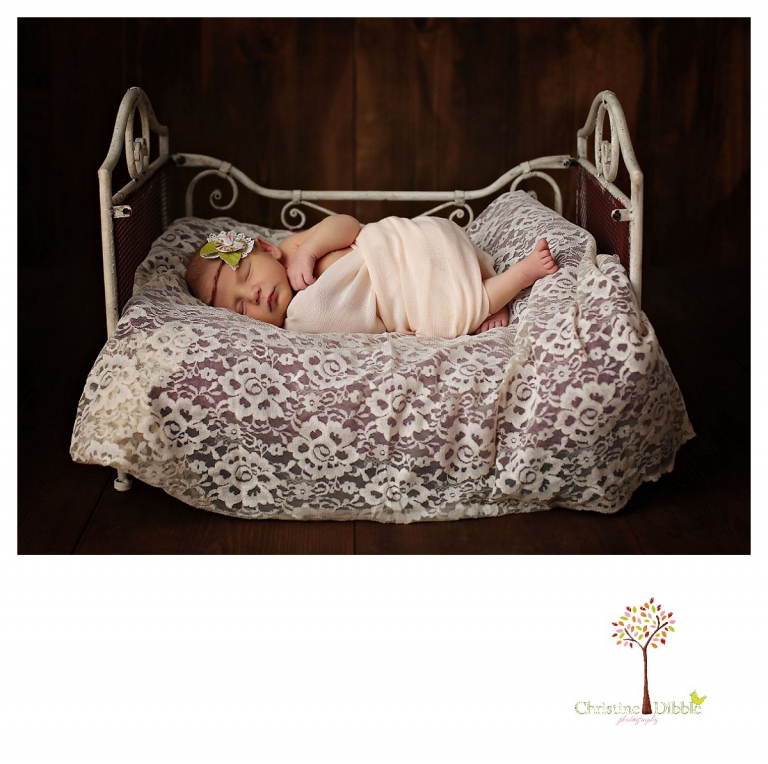Sonora newborn photographer Christine Dibble Photography takes photos of a baby girl wearing a flower and a wrap and sleeping in a tiny iron bed.