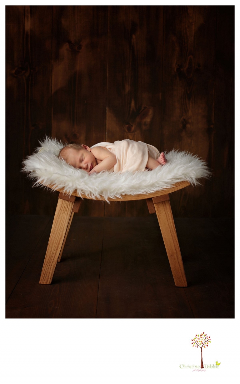 Sonora newborn photographer Christine Dibble Photography takes photos of a baby girl sleeping on a hand crafted curved oak stool and fur.