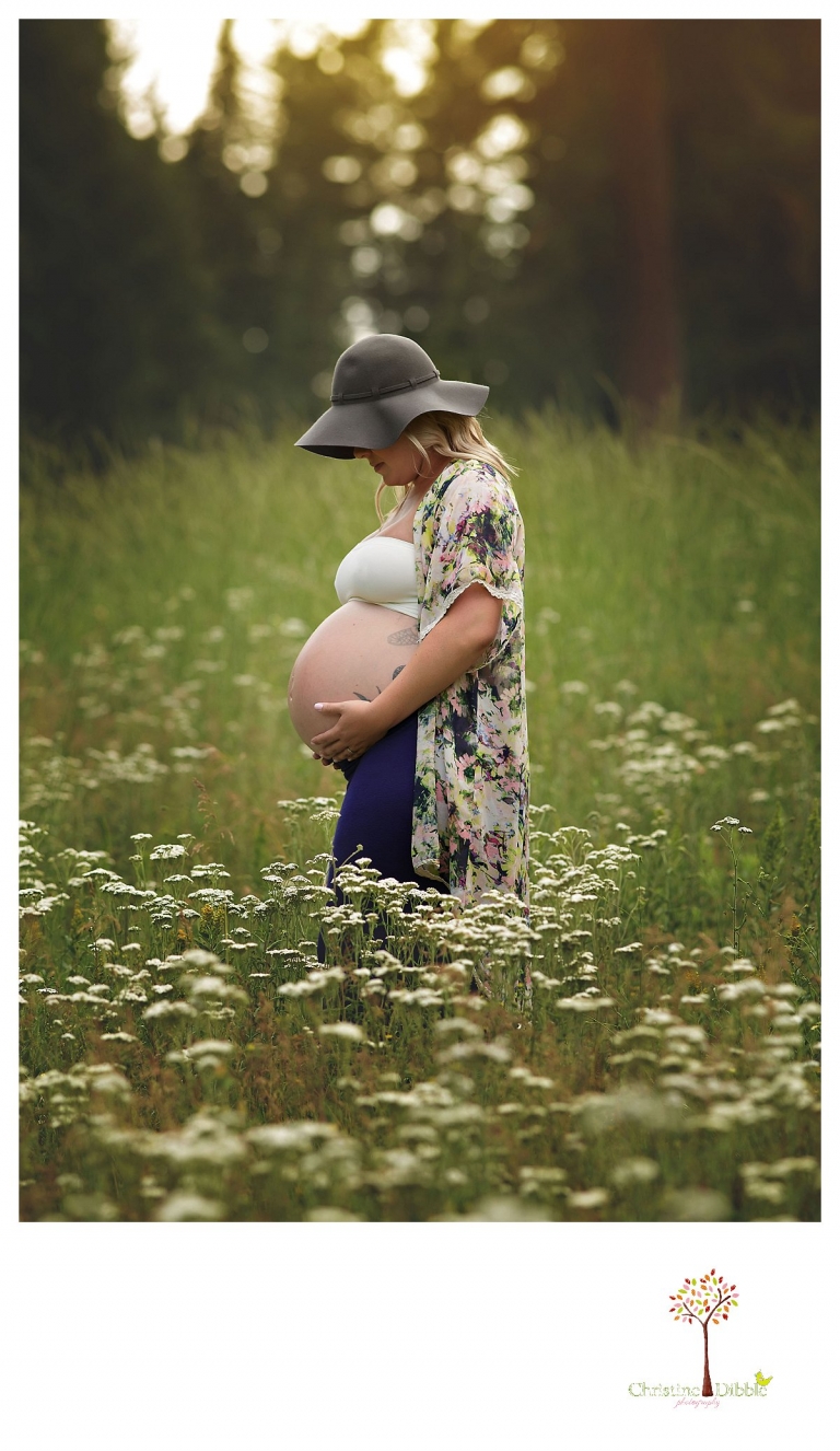 Sonora maternity photographer Christine Dibble Photography takes pregnancy photos of a tattooed mom in a field of wildflowers wearing a maxi skirt, floral kimono top and a floppy hat.