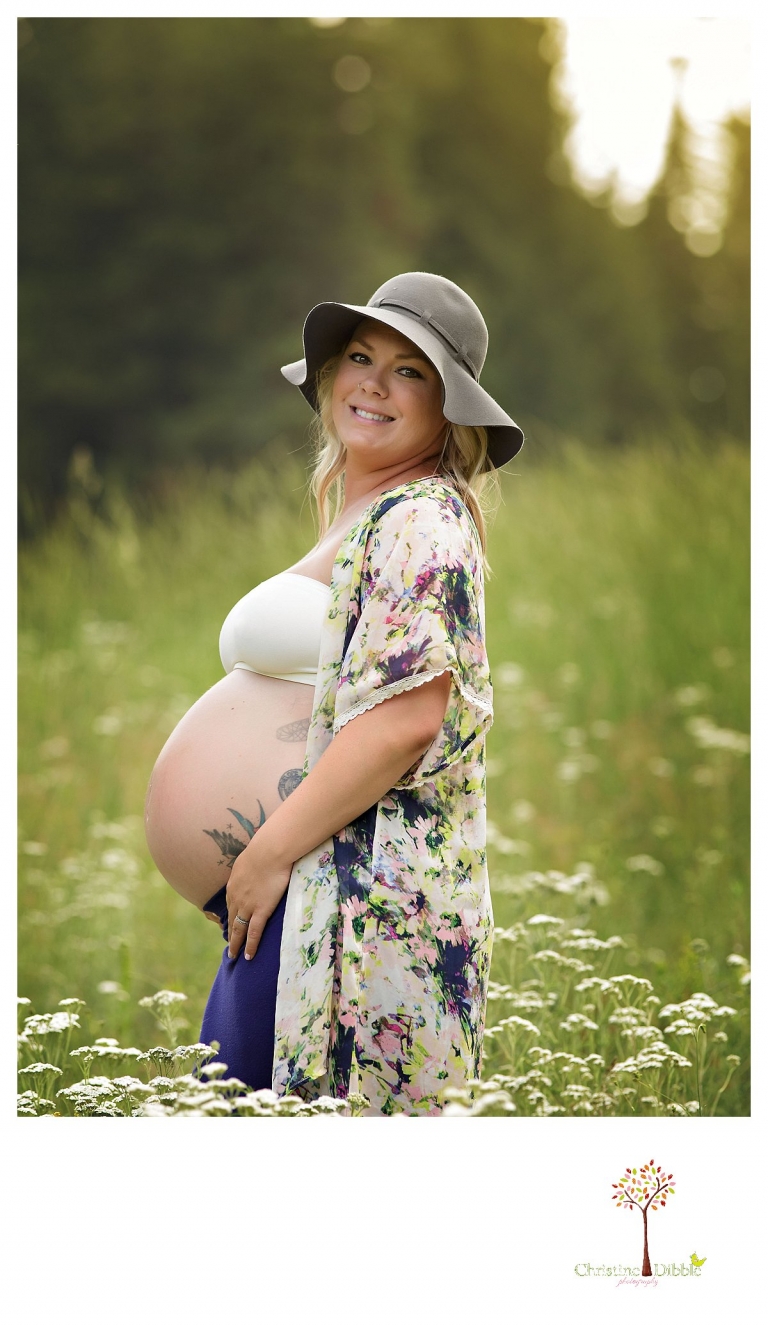 Sonora maternity photographer Christine Dibble Photography takes pregnancy photos of a mom with belly tattoos in a flower field while wearing a skirt, loose top and hat.