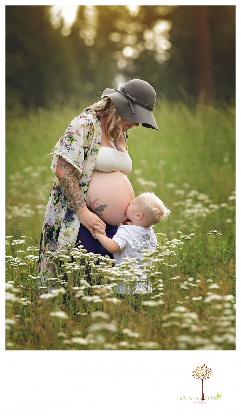 Sonora maternity photographer Christine Dibble Photography takes pregnancy photos of a mom as her toddler son kisses her baby belly bump in a field of wildflowers.