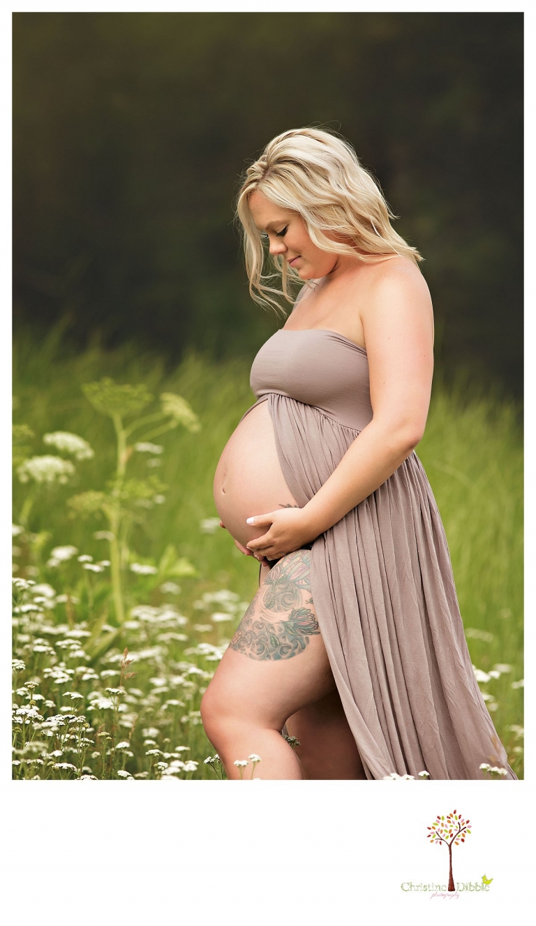 Sonora maternity photographer Christine Dibble Photography takes photos of a pregnant mother with tattooed legs as she poses in a belly dress in a wildflower field.
