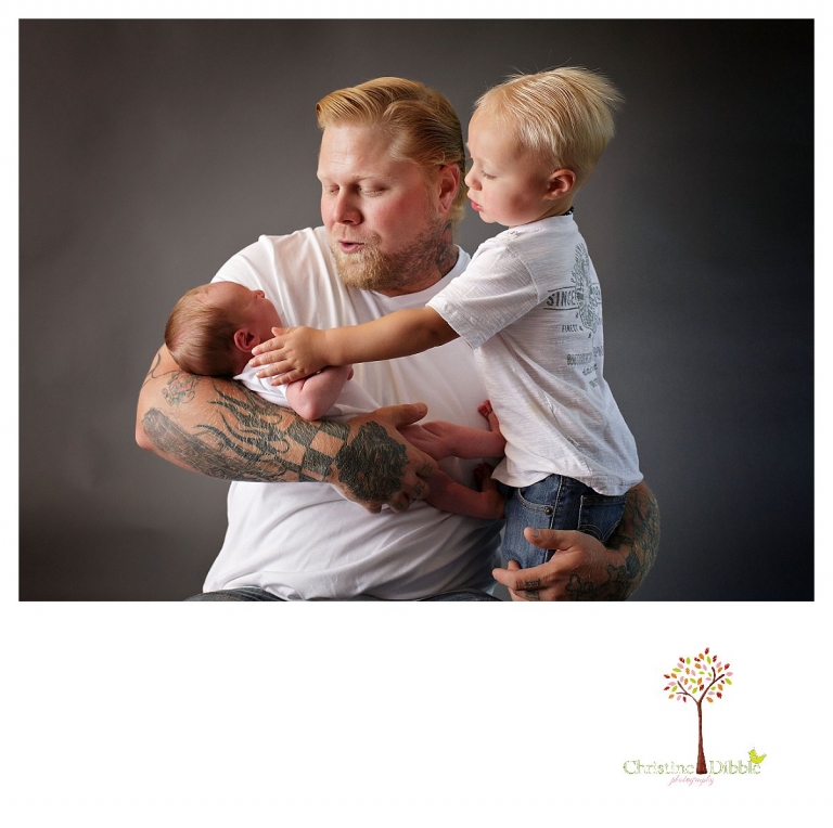 Sonora newborn and family photographer Christine Dibble Photography takes a portrait of a big brother reaching out to calm his crying newborn baby brother while dad helps during a newborn and family portrait session in the Sonora studio.