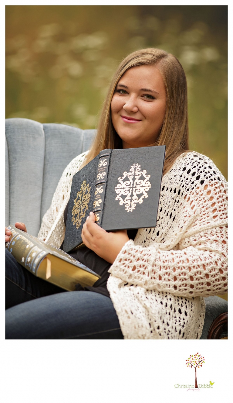 Sonora and Summerville senior portrait photographer Christine Dibble Photography takes outdoor senior portraits of a girl reading books in a blue velvet chair in a flower field.