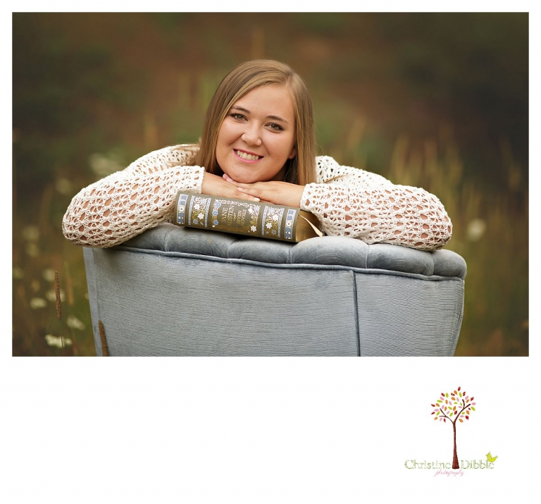 Sonora and Summerville senior portrait photographer Christine Dibble Photography takes outdoor senior portraits of a girl with her books in a blue velvet chair in a field.